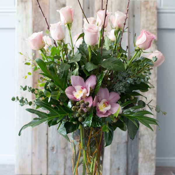 Pink roses and orchids arranged in a tall glass vase