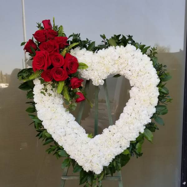 Heart-shaped floral wreath with white blooms and red roses on an easel