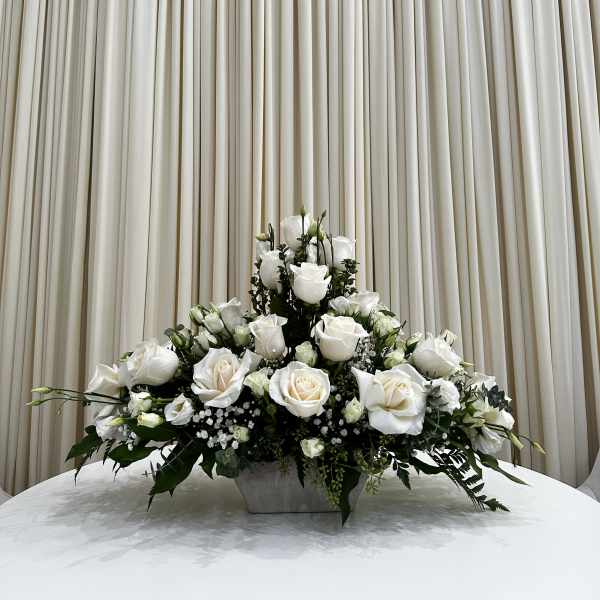 Low arrangement of white roses with small white filler flowers in a rectangular vase on a round table