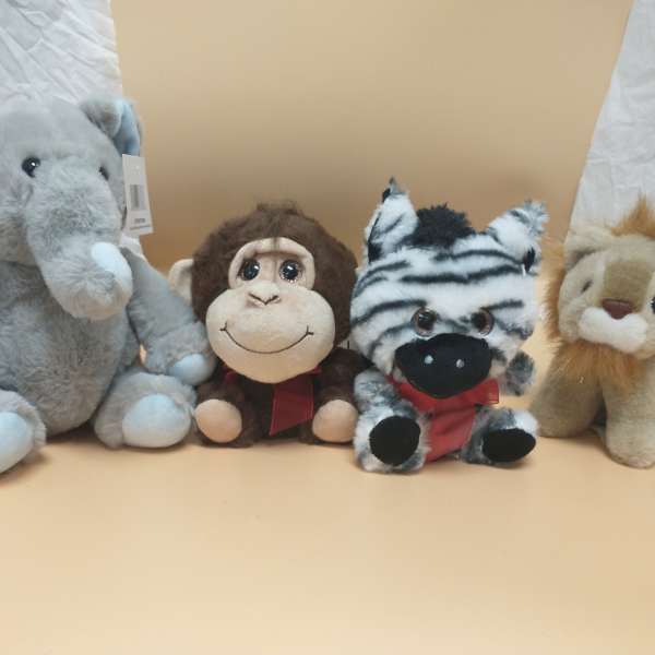 Four plush animals arranged side by side, including an elephant, monkey, zebra, and lion.