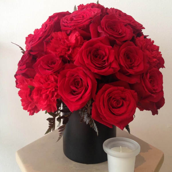 Red roses and carnations arranged in a black vase beside a white candle.