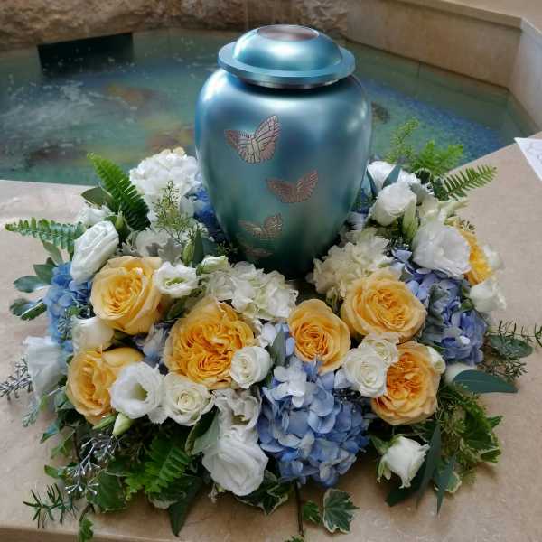 Floral funeral urn arrangement with yellow roses, white blooms, and blue hydrangeas