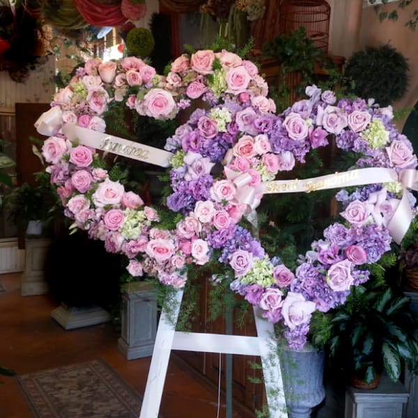 Two heart-shaped floral wreaths of pink and lavender roses on easels