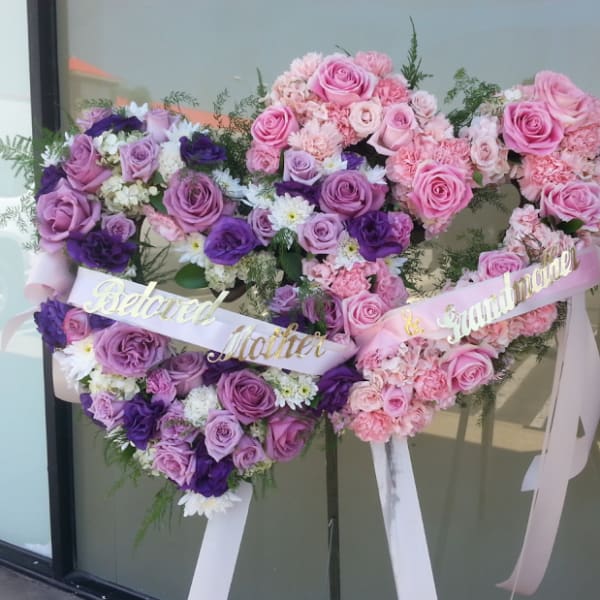 Heart-shaped floral tribute with pink and purple roses and ribbons