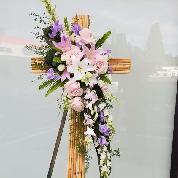 Floral cross arrangement with pink and purple flowers on a bamboo cross stand