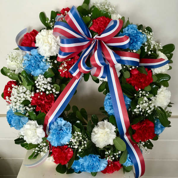 Round floral wreath with red, white, and blue carnations and a striped ribbon bow