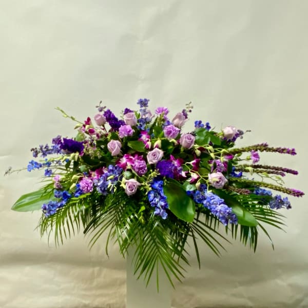 Large purple and blue floral arrangement in a white pedestal vase
