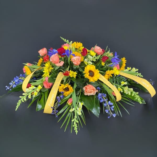 Colorful floral casket spray with roses, sunflowers, and blue accents