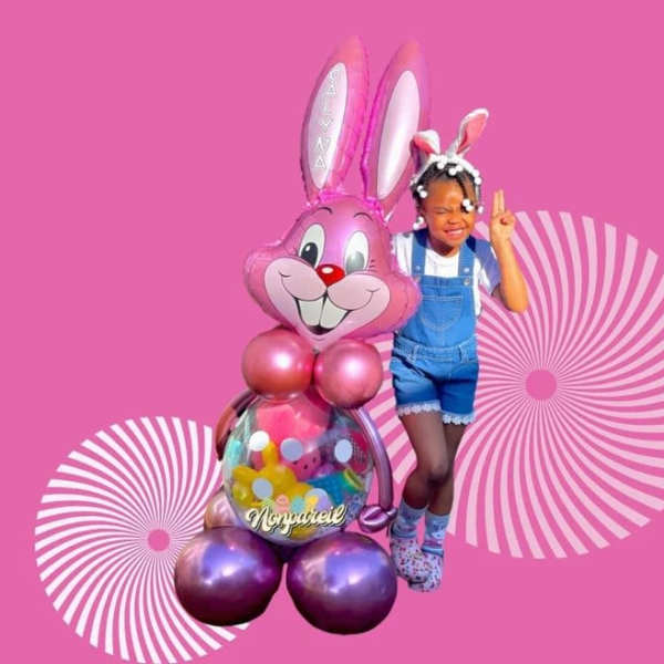 Girl posing beside a pink bunny balloon sculpture on a pink background