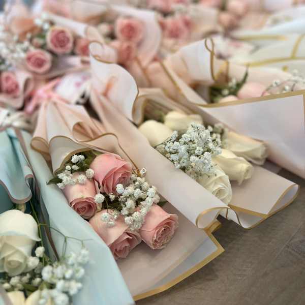 Several pastel rose bouquets wrapped in paper with baby's breath