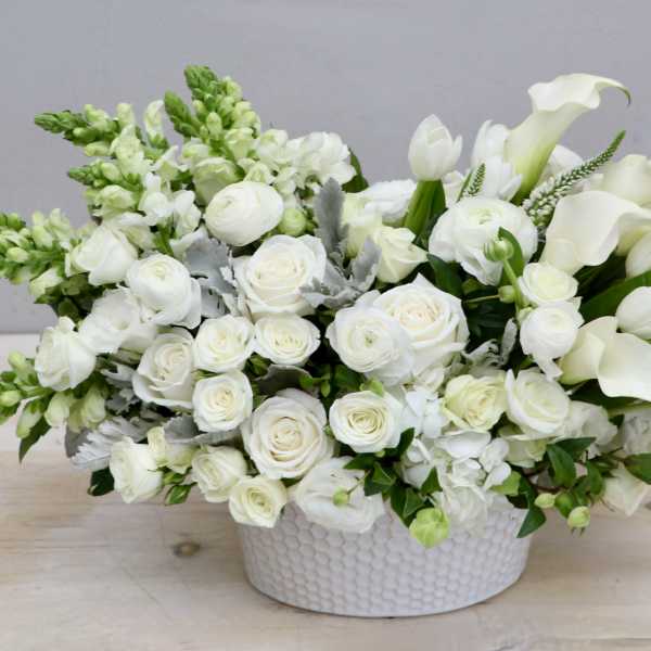 Low white arrangement of roses, calla lilies, tulips, and snapdragons in a round ceramic bowl