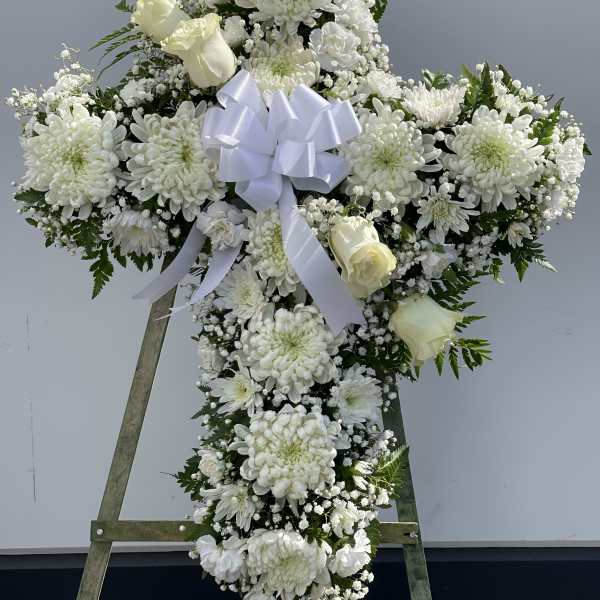 White floral cross wreath with a ribbon bow on an easel