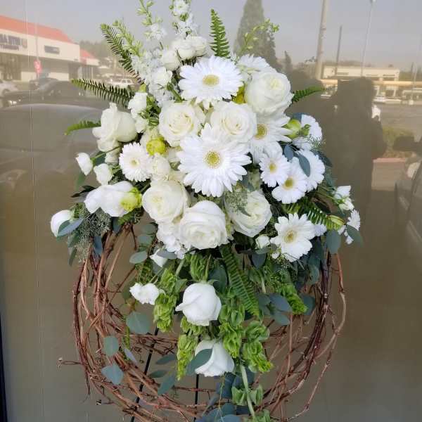 White floral standing arrangement with roses and daisies on a twig wreath stand
