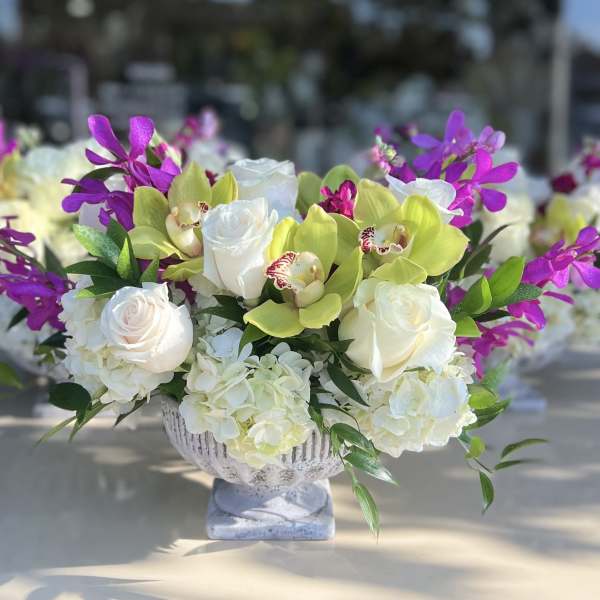 White roses and hydrangeas with purple orchids in a pedestal vase