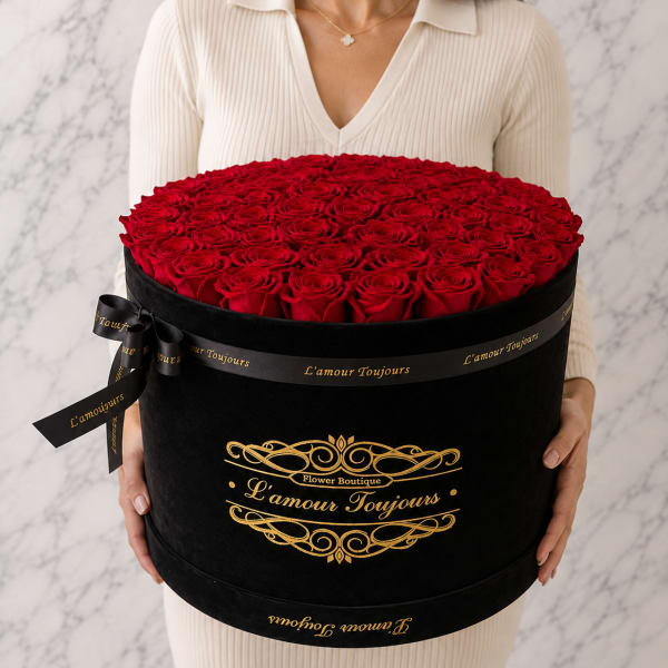 Woman holding a large round box of red roses with a black ribbon