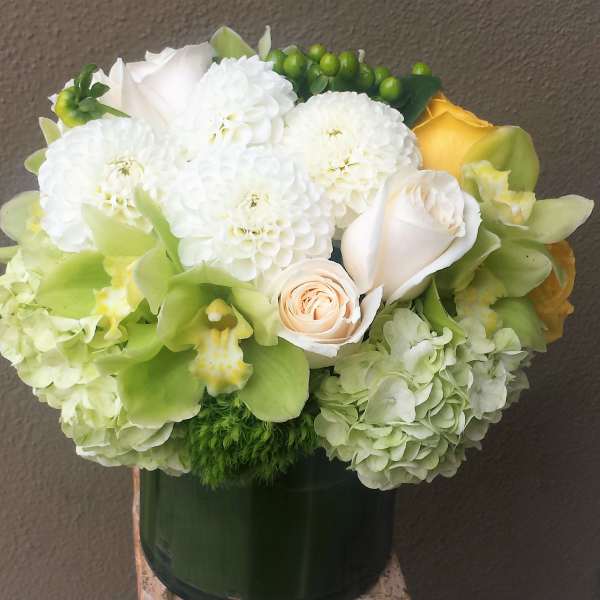 White and green floral arrangement with roses and orchids in a dark vase