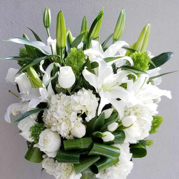 White lilies and roses arranged in a tall green glass vase