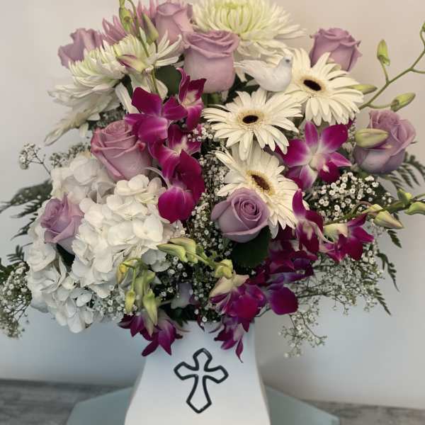 Lavender roses and white daisies in a white vase with a cross emblem