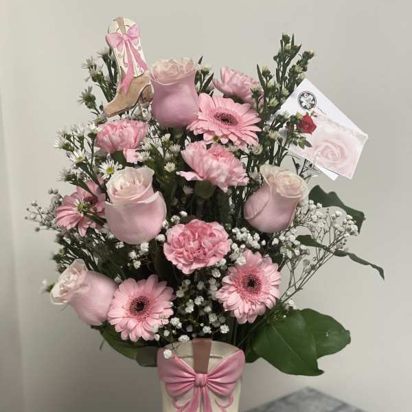 Pink flower arrangement in a decorative boot vase with a bow