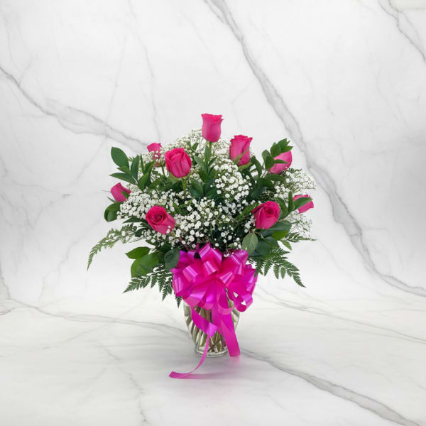Pink roses and baby's breath in a glass vase with a magenta bow