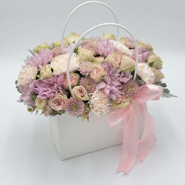 Pink and cream flowers arranged in a white handled box with a pink ribbon