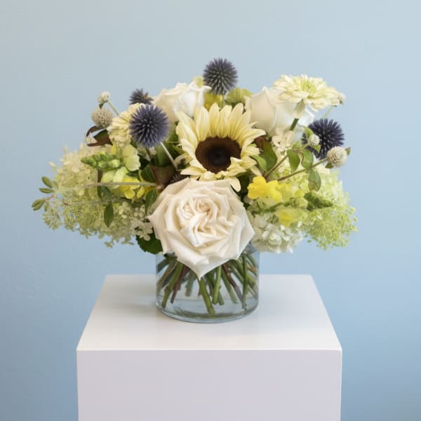 White roses and a sunflower in a glass vase with blue thistle accents