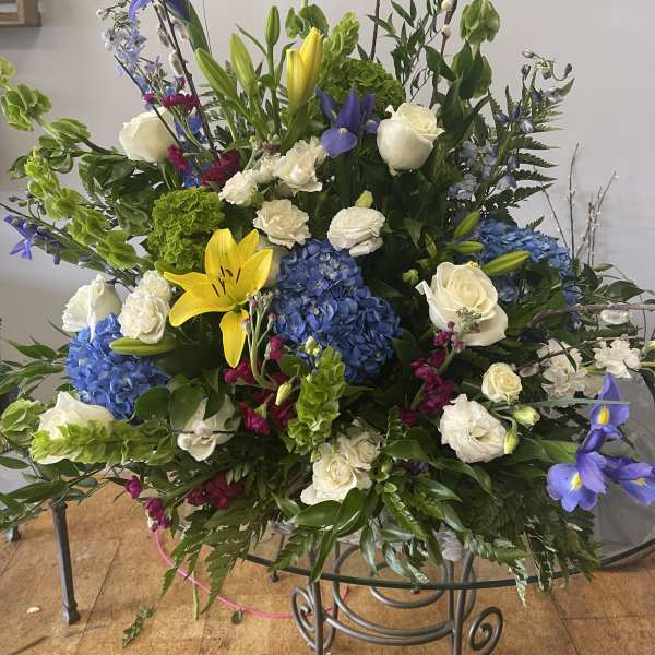 Large mixed floral arrangement with blue hydrangeas, white roses, and yellow lilies