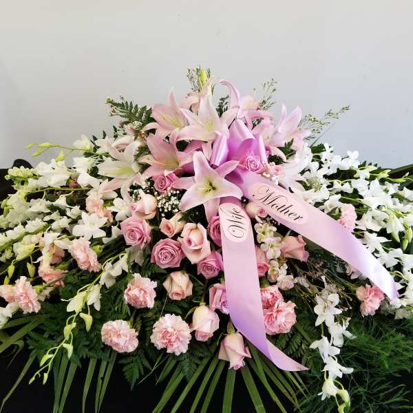 Pink lilies and roses arranged with white orchids and ribbons
