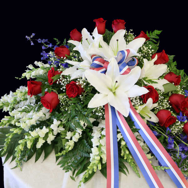 Large funeral spray of red roses and white lilies with a tricolor ribbon