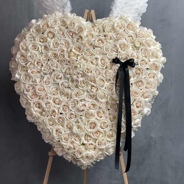 Heart-shaped rose arrangement with white wings and a black ribbon on an easel