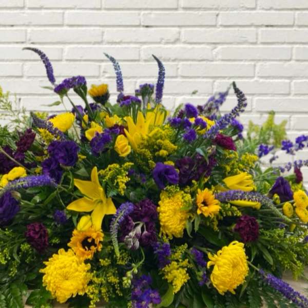 Large yellow and purple floral arrangement against a white brick wall