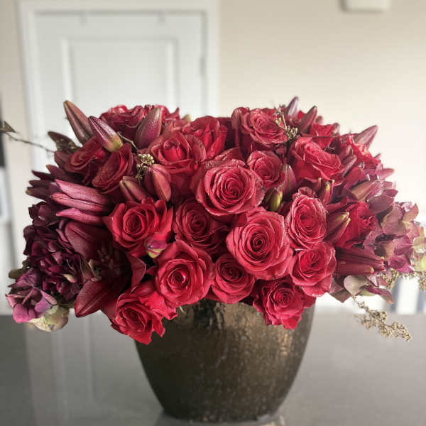 Red roses and dark lilies arranged in a dark vase