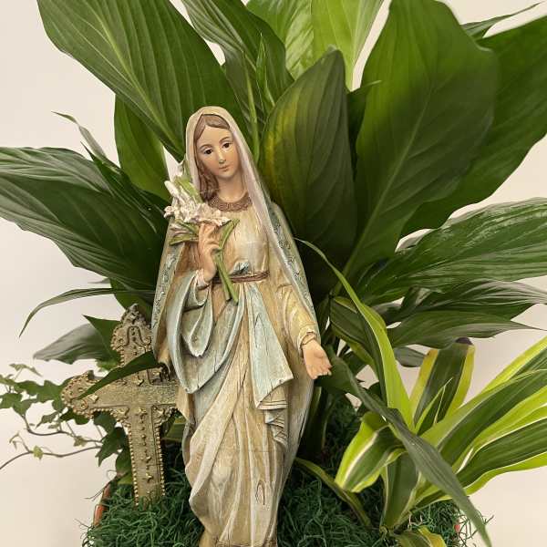 Potted religious statue surrounded by broad green foliage