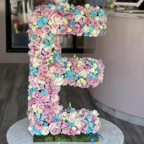 Large letter E covered in pastel roses with butterfly accents