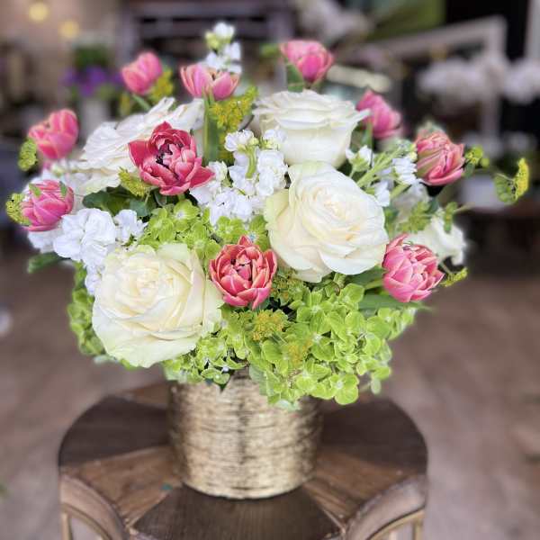 Pink and white roses arranged in a gold vase with green hydrangea accents