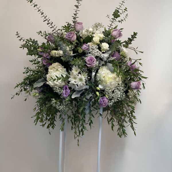 Lavender and white floral arrangement on a tall stand with candles below