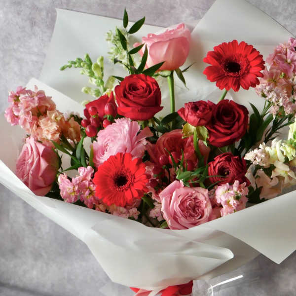 Bouquet of pink and red roses with gerbera daisies and mixed blooms wrapped in white paper