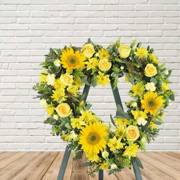 Heart-shaped floral wreath with yellow sunflowers and roses on a stand
