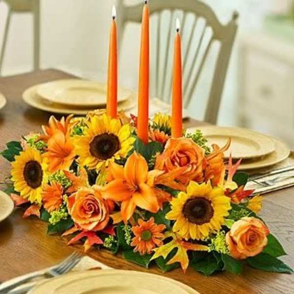 Orange floral centerpiece with tall candles on a dining table