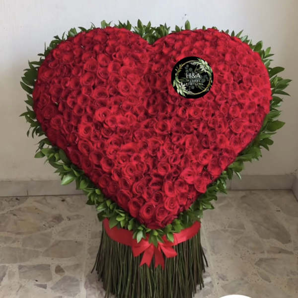Heart-shaped arrangement of red roses with a green border and red ribbon