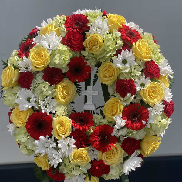 Circular floral wreath with red, yellow, and white blooms and a small cross