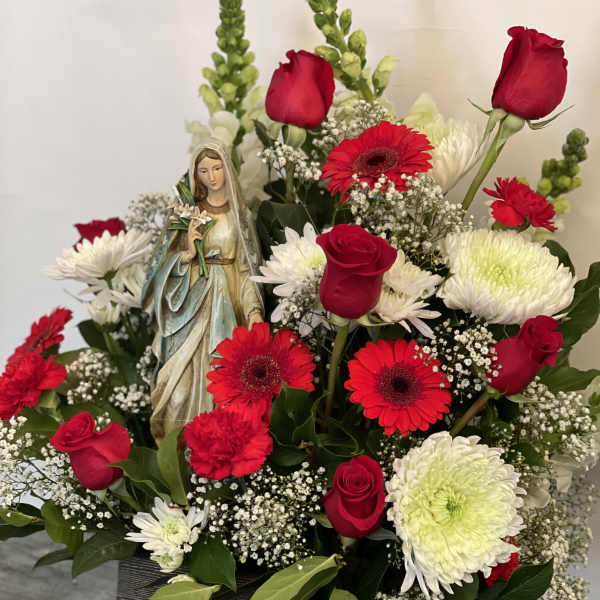 Red roses and gerbera daisies arranged around a small statue in a box.