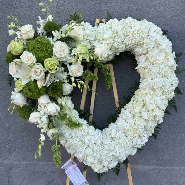 Heart-shaped floral wreath with white flowers and green accents on an easel