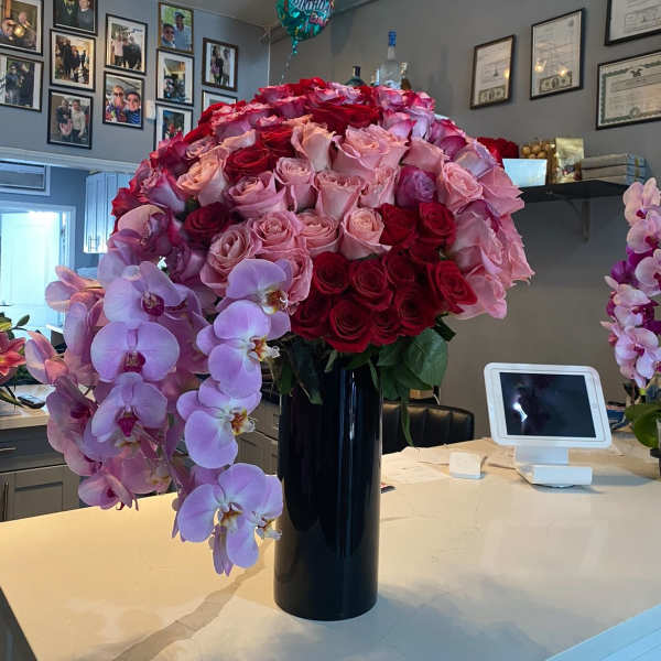 Tall arrangement of red and pink roses with cascading pink orchids in a black vase