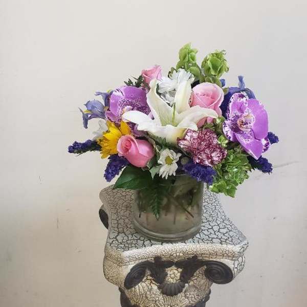 Mixed bouquet with white lilies, pink roses, and purple orchids in a glass vase