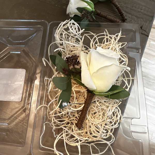 White rose boutonnieres in clear plastic packaging with straw filler.