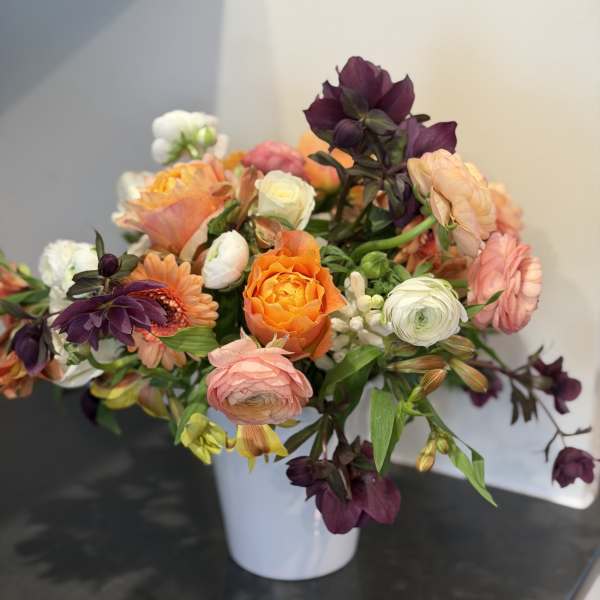 Mixed bouquet of orange, pink, white, and purple flowers in a white vase