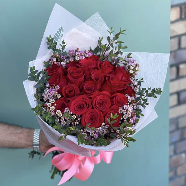 Bouquet of red roses with small pink filler flowers and white wrapping