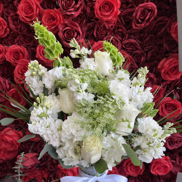 White bouquet in a glass vase with a white ribbon, set against red roses