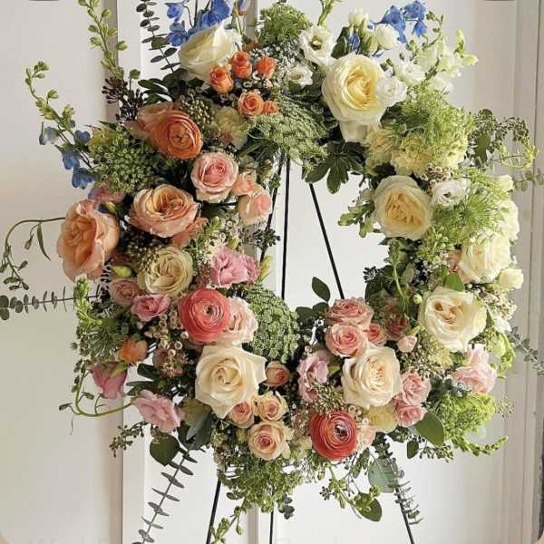 Circular floral wreath with roses, ranunculus, and blue flowers on a stand
